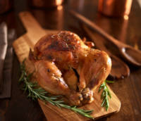 rotisserie chicken on wooden serving tray with herbs and rosemary