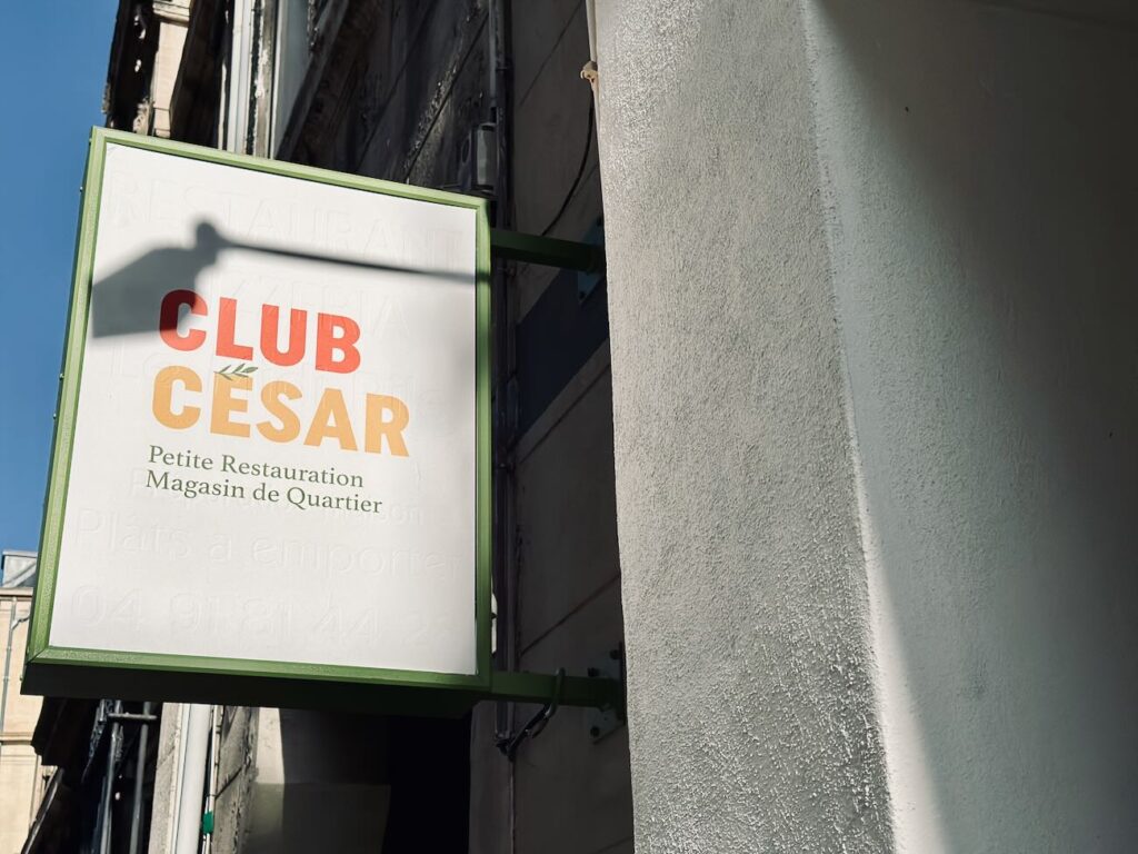 Club César est une cantine de quartier où il est possible de s’attabler pour un café, un déjeuner et un goûter. L’adresse dispose également d’une offre épicerie. (enseigne)