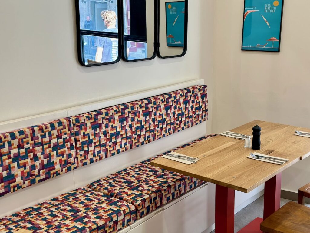 Club César est une cantine de quartier où il est possible de s’attabler pour un café, un déjeuner et un goûter. L’adresse dispose également d’une offre épicerie. (banquette)